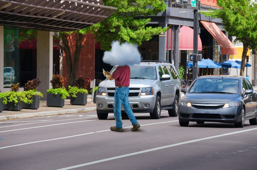 Man distracted by phone jaywalks into traffic, head in the clouds.