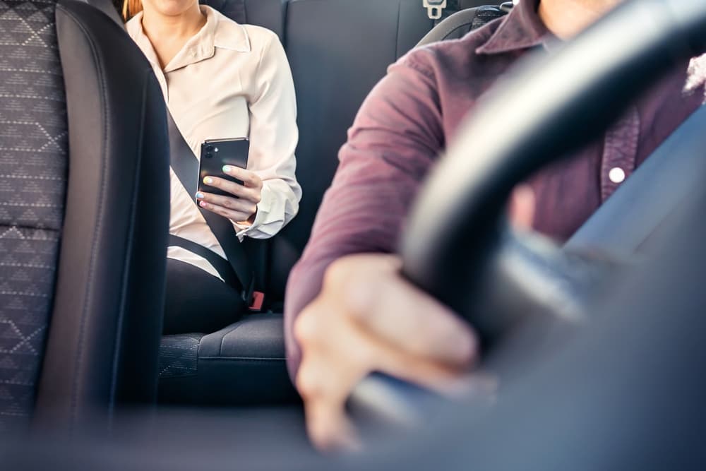 Woman using phone in backseat of rideshare on commute to work.