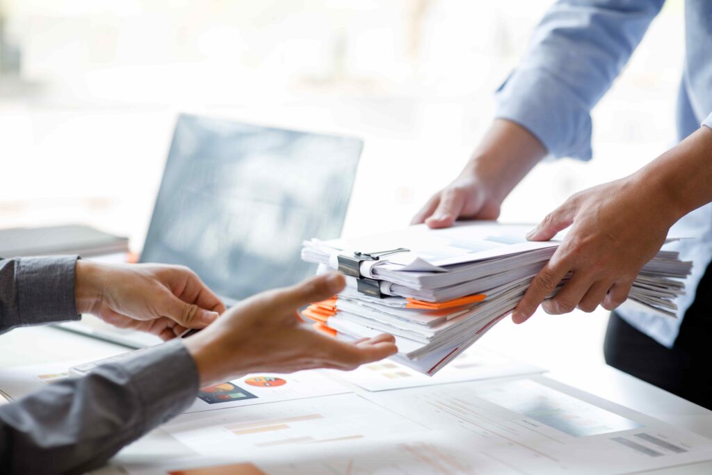 Business professionals exchanging stack of documents and reports at office desk Business professionals exchanging stack of documents and reports at office desk