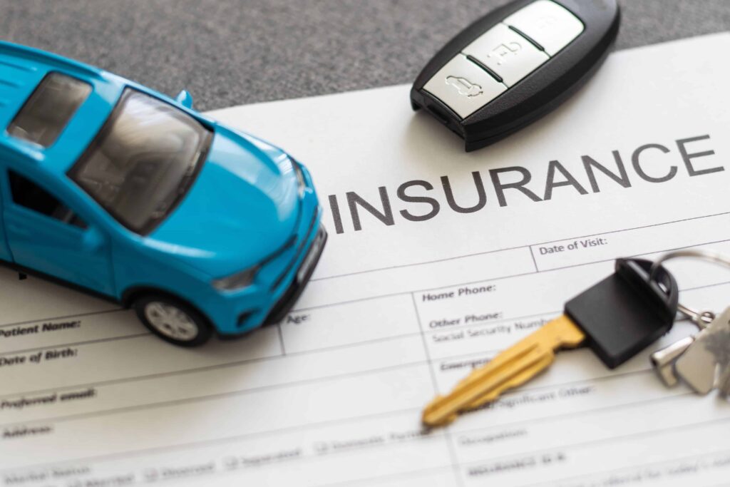 Car insurance document with toy car, car keys, and remote key fob on desk