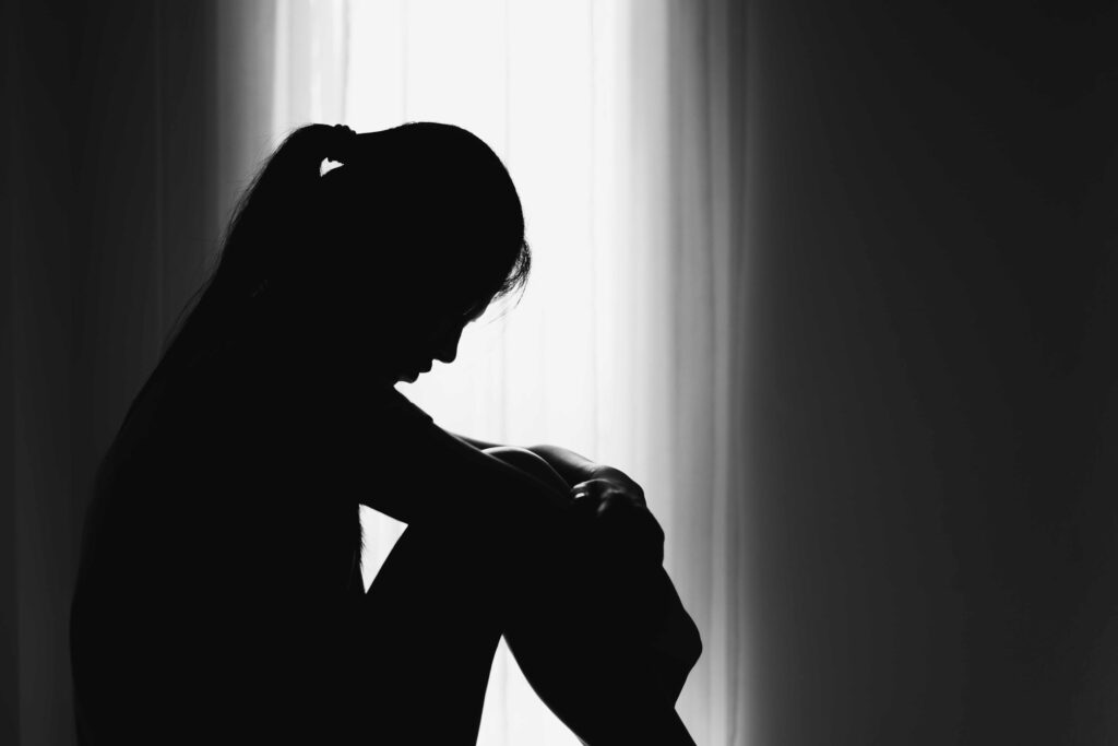Silhouette of sad woman sitting alone in dark room symbolizing depression and emotional distress Silhouette of sad woman sitting alone in dark room symbolizing depression and emotional distress