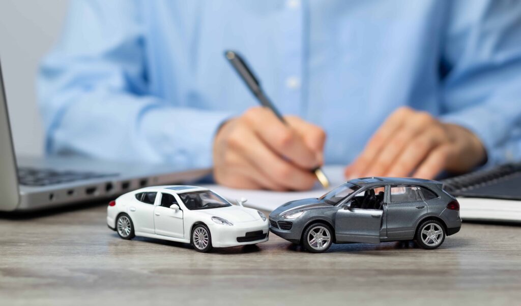 Insurance agent writing report with car accident model vehicles on desk